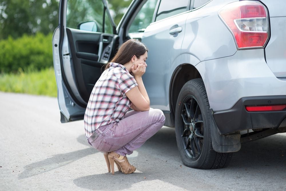 Woman looking at a flat tire on her car