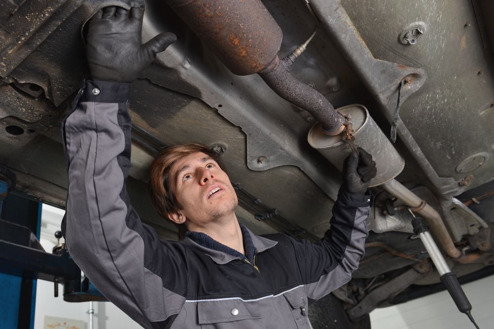 Mechanic inspecting the catalytic converter (left) and muffler (right) prior to straight piping a car